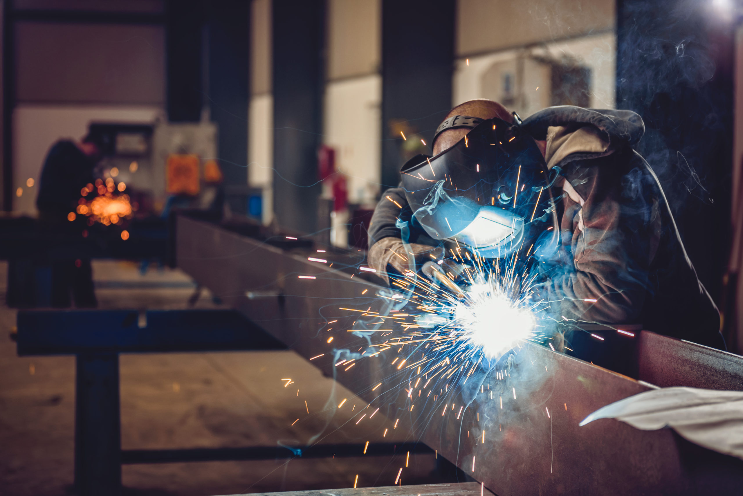 Industrial,Welder,With,Torch,And,Protective,Helmet,In,Big,Hall